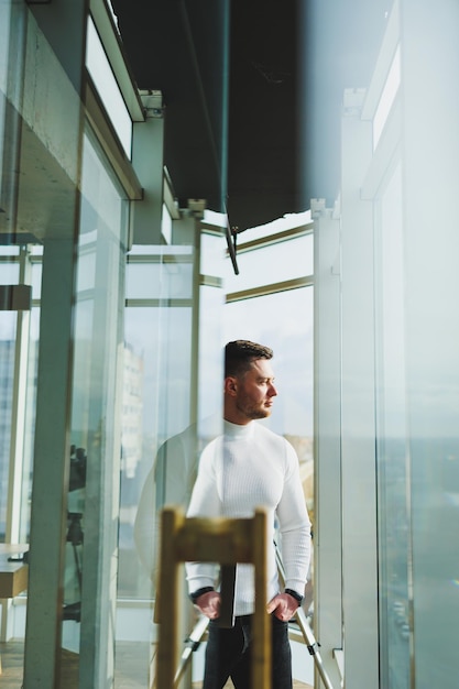 A young man in a modern workspace stands near a large window A man in casual clothes with a laptop in his hands Remote work Nice young manager