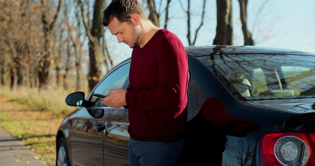 A young man near a broken car uses a mobile phone to call an emergency service. Concept road accident. Help repair.