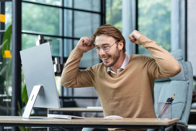 Young man in office celebrating victory and successful achievement results businessman holding hands