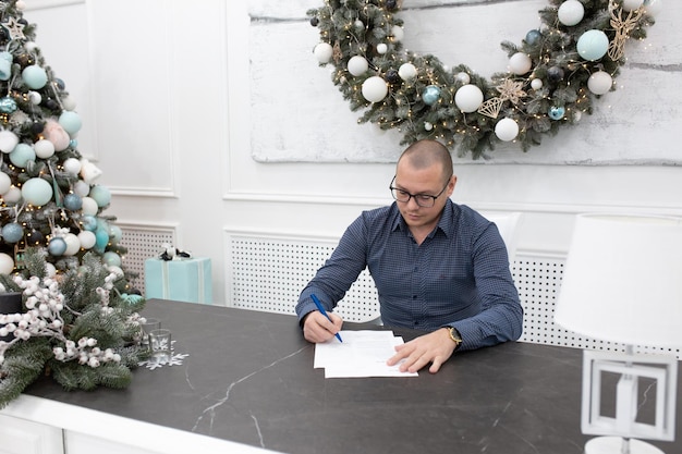 a young man in the office at the table signs documents. office with Christmas decor. festive mood in