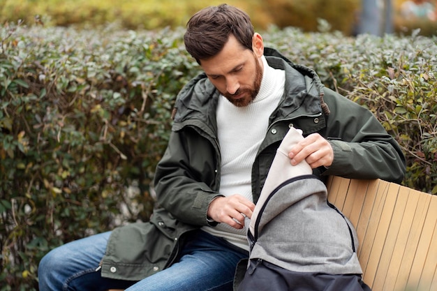 Young man opening his backpack A man sits on a bench in a city park