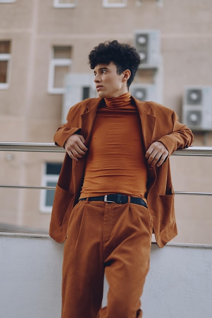 Young man in an orange outfit against a muted wall backdrop exuding confidence and contemporary