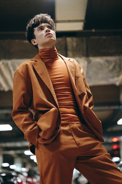 Photo a young man in an orange suit posing thoughtfully in an urban parking garage setting