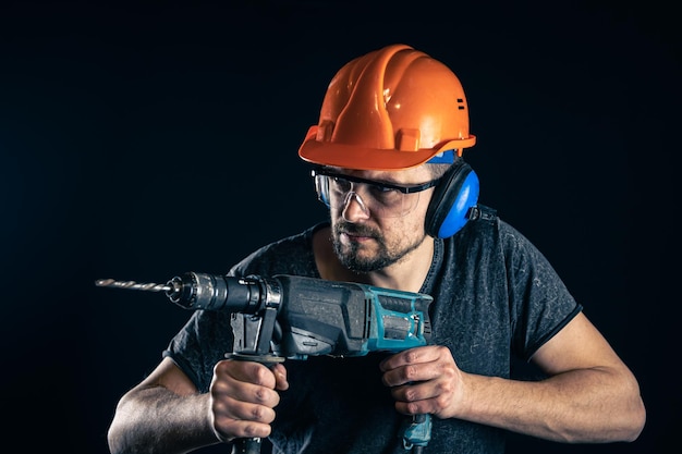 A young man in overalls protective helmet hard hat hold electric drill