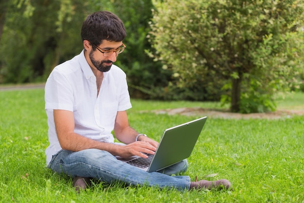 Young man in the park sitting on the grass with a laptop