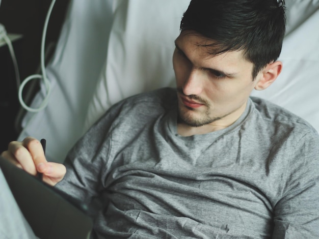 Photo young man patient with a tablet lying in the hospital ward