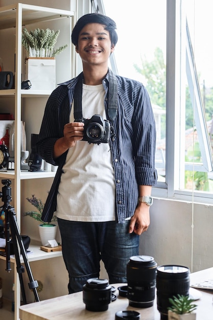 Young man photographer with  professional camera smiling against home office studio background.