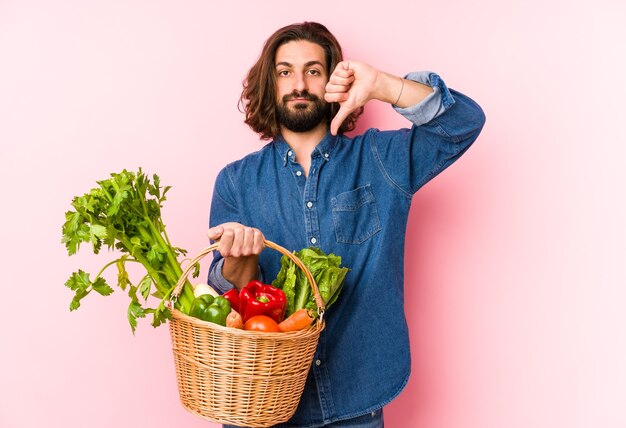 Young man picking organic vegetables from his garden isolated showing a dislike gesture, thumbs down. Disagreement concept.