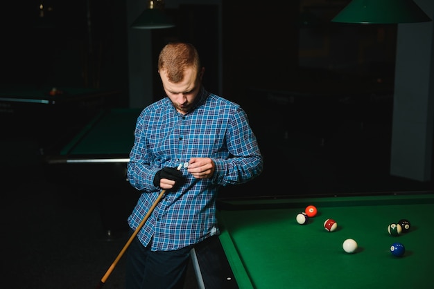 Young man playing billiards in the dark billiard club