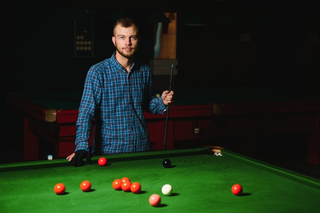 Young man playing billiards in the dark billiard club