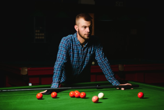 Young man playing billiards in the dark billiard club