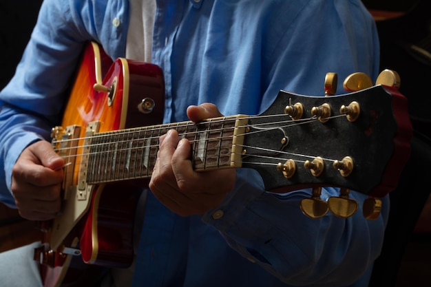 Young man playing guitar close up view dark background