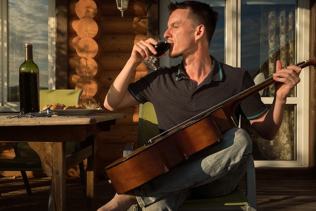 Young man playing guitar and drinking wine alone. Covid-19 quarantine.