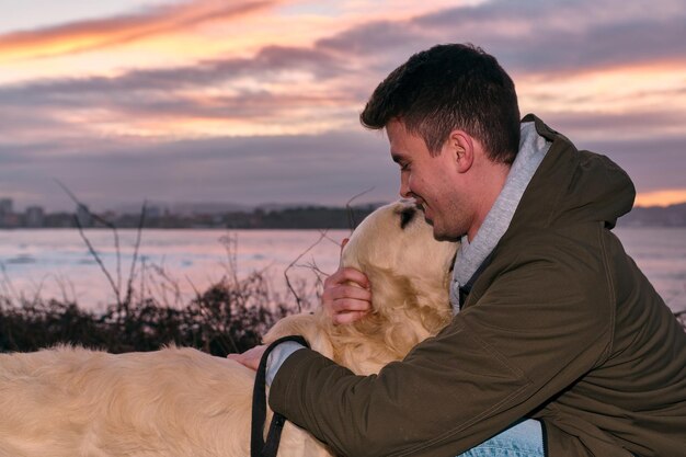 Young man playing and hugging his golden retriever dog at a sunset