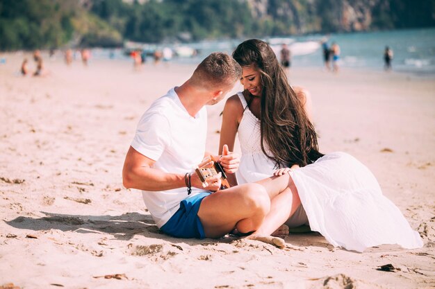 Photo young man playing ukulele while sitting with girlfriend at beach