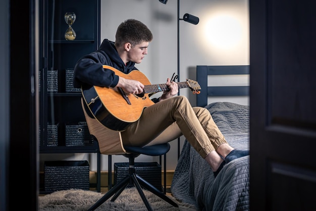 A young man plays the acoustic guitar in his room at home