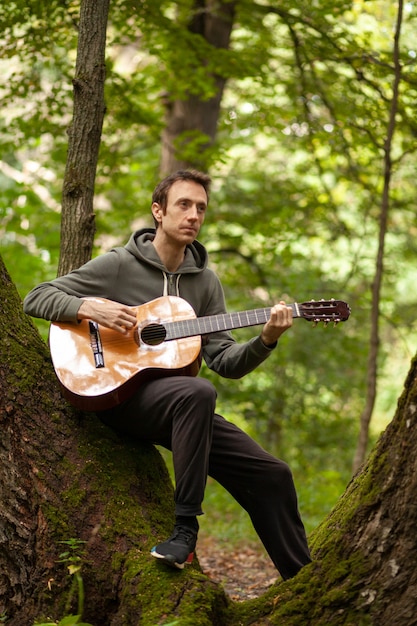 Young man plays acoustic guitar on nature in forest