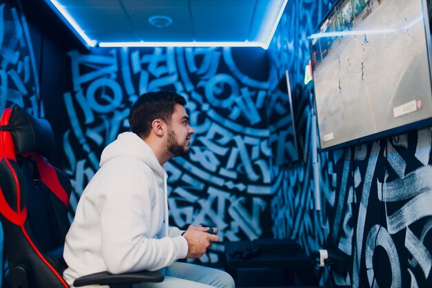 Young man plays on game console with gamepad sitting on chair