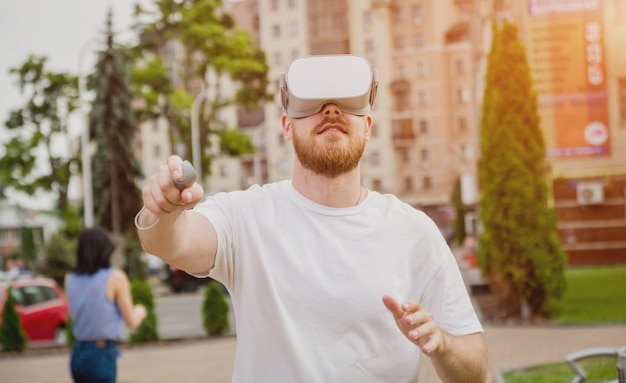 A young man plays a game wearing virtual reality glasses on the street.