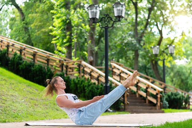 Young man practice yoga in the park. Yoga asanas in city park, sunny day. Concept of meditation, wellbeing and healthy lifestyle