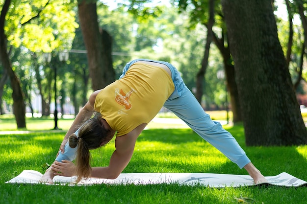 Young man practice yoga in the park. Yoga asanas in city park, sunny day. Concept of meditation, wellbeing and healthy lifestyle