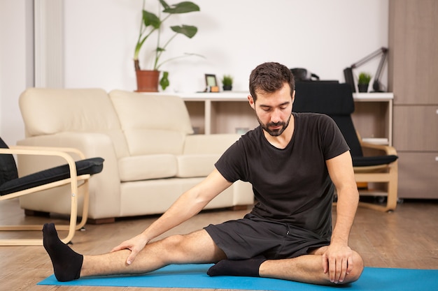 Young man practicing yoga in his living room at home. He is strecking and feels relaxed