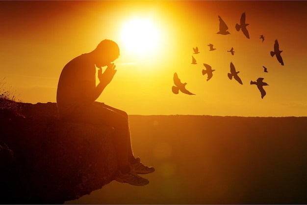 Young man pray outdoor on top of mountains in sunset