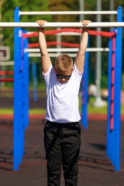 A young man pulls up on a horizontal bar on a sports ground in the summer. High quality photo