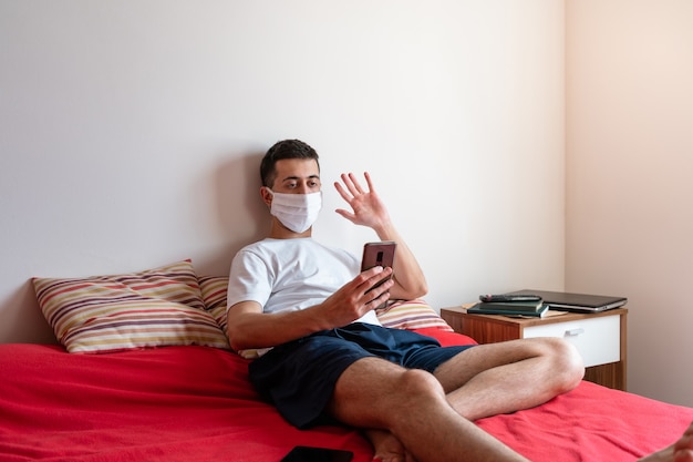 Young man in quarantine making a video call with family members from bed