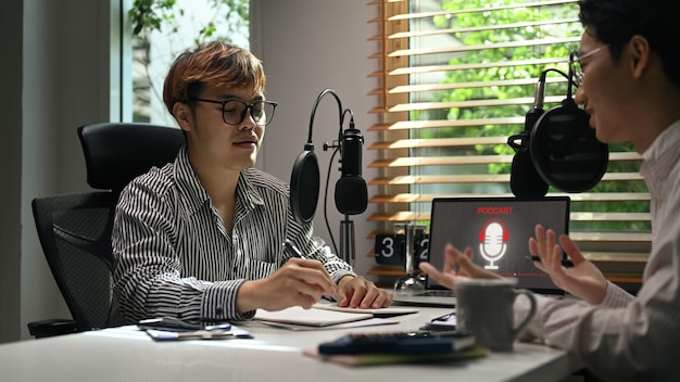 Young man radio host interviewing guest in studio while recording live podcast in studio Radio podcasts blogging and technology concept