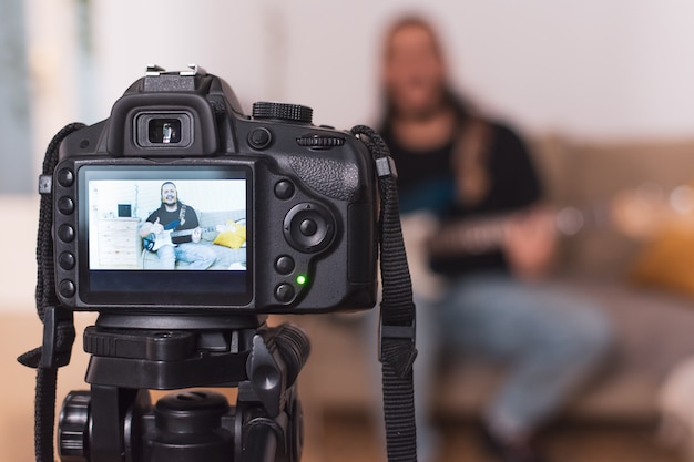 Young man recording an online guitar lesson video tutorial at home