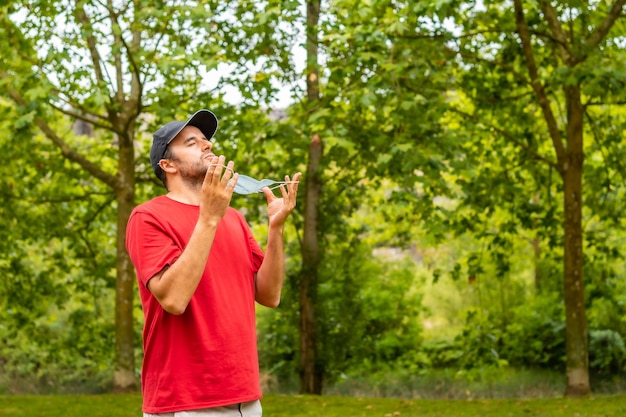 Young man in a red t-shirt removing his surgical mask with trees background