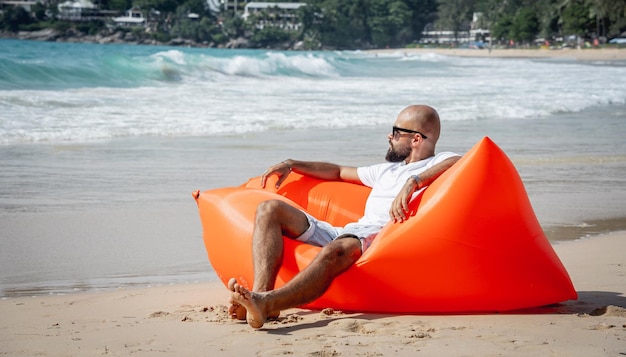 Young man relaxing on the beach while sitting on an inflatable sofa