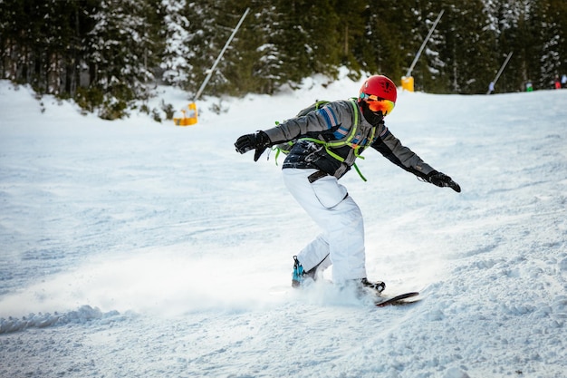 Young man rides snowboard and enjoying a sunny winter day on mountain slopes.