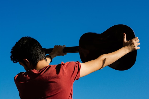 Young man rising an accoustic guitar in the sky