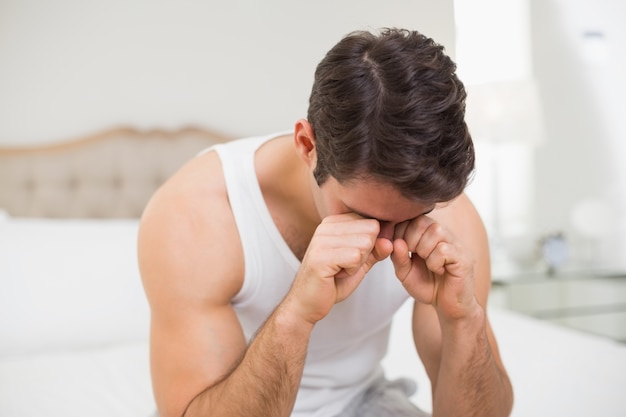 Young man rubbing his eyes in bed