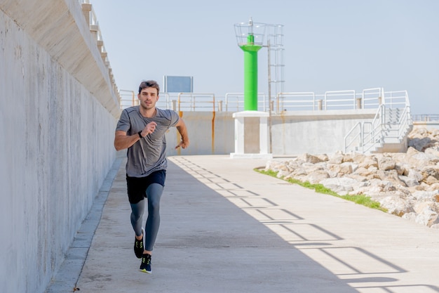 Young man running along a promenade near a harbor lighthouse