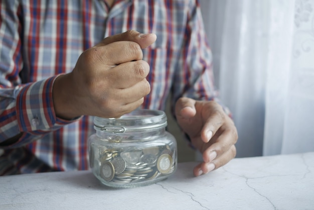 Young man saving coins in a jar white sited