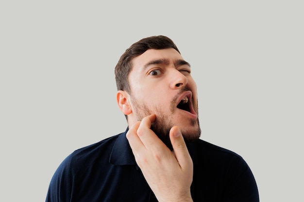 Young man scratching bearded bearded guy scratching his beard in the studio on a gray background tho