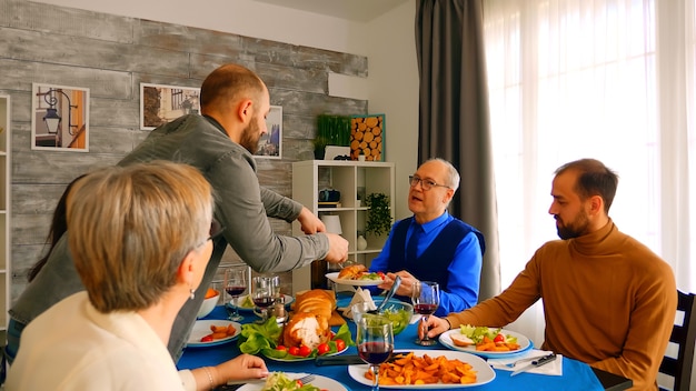 Young man serving his father with a big slice of chicken at dinner.