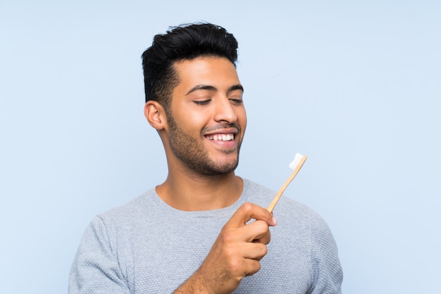 Young man shaving his beard over isolated blue wall