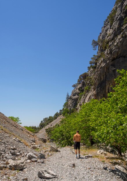 Young man in shorts and a baseball cap walks through a mountain gorge in Greece