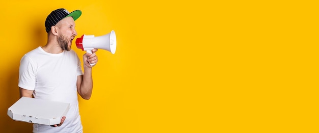 Young man shouting into a megaphone holding packed pizza on a yellow background Banner