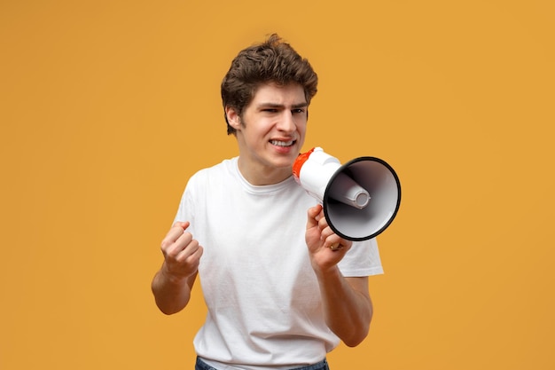 Young man shouting into megaphone making announcement against yellow background