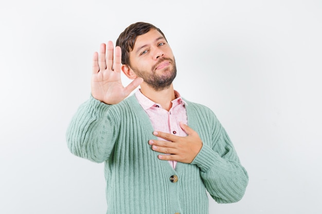 Young man showing stop gesture, keeping hand on chest in shirt, cardigan and looking grateful , front view.