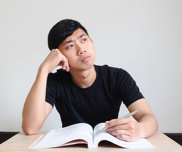 Young man sit at the desk confused with the book in hand on white isolated