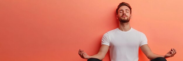 Photo a young man sits in a relaxed yoga pose eyes closed against a vibrant coral wall symbolizing