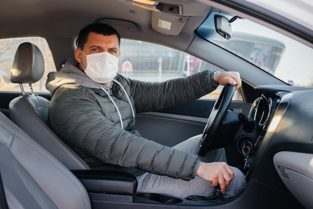 A young man sits behind the wheel wearing a mask for personal safety while driving during a pandemic and coronavirus. Epidemic.