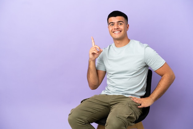 Young man sitting on a chair over isolated background pointing with the index finger a great idea