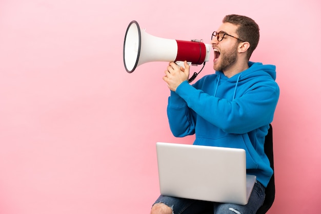 Young man sitting on a chair with laptop shouting through a megaphone